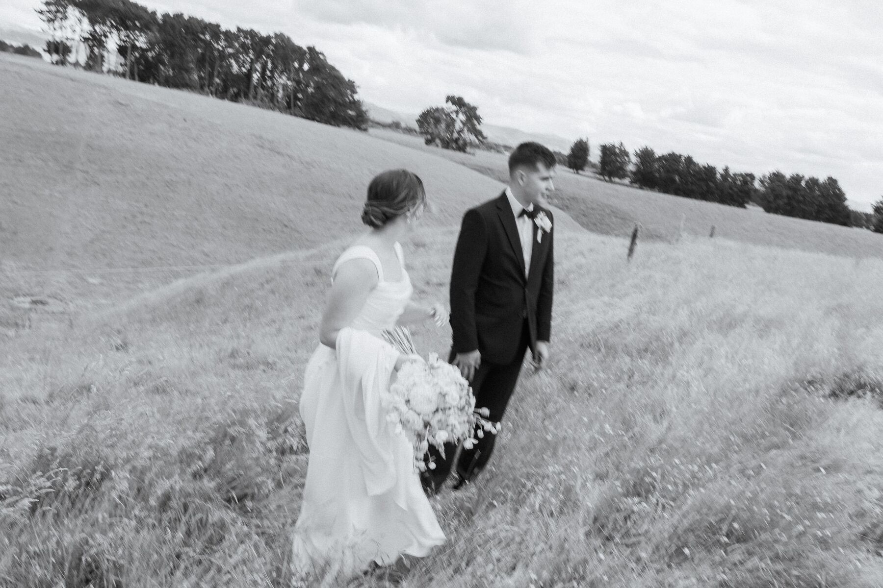 A couple walking through a New Zealand field, photographed in black and white