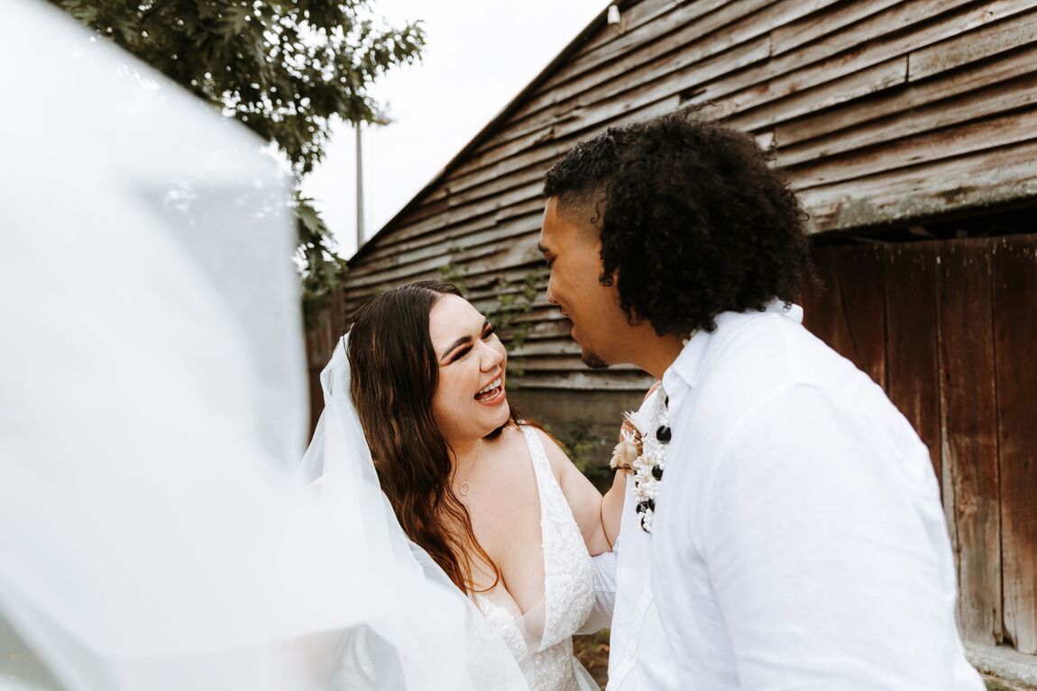 Bride and groom laughing together beside a wooden barn