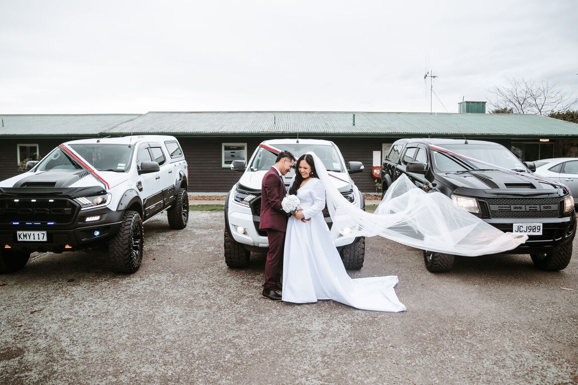 Couple with a veil catching the wind beside utes in rural New Zealand