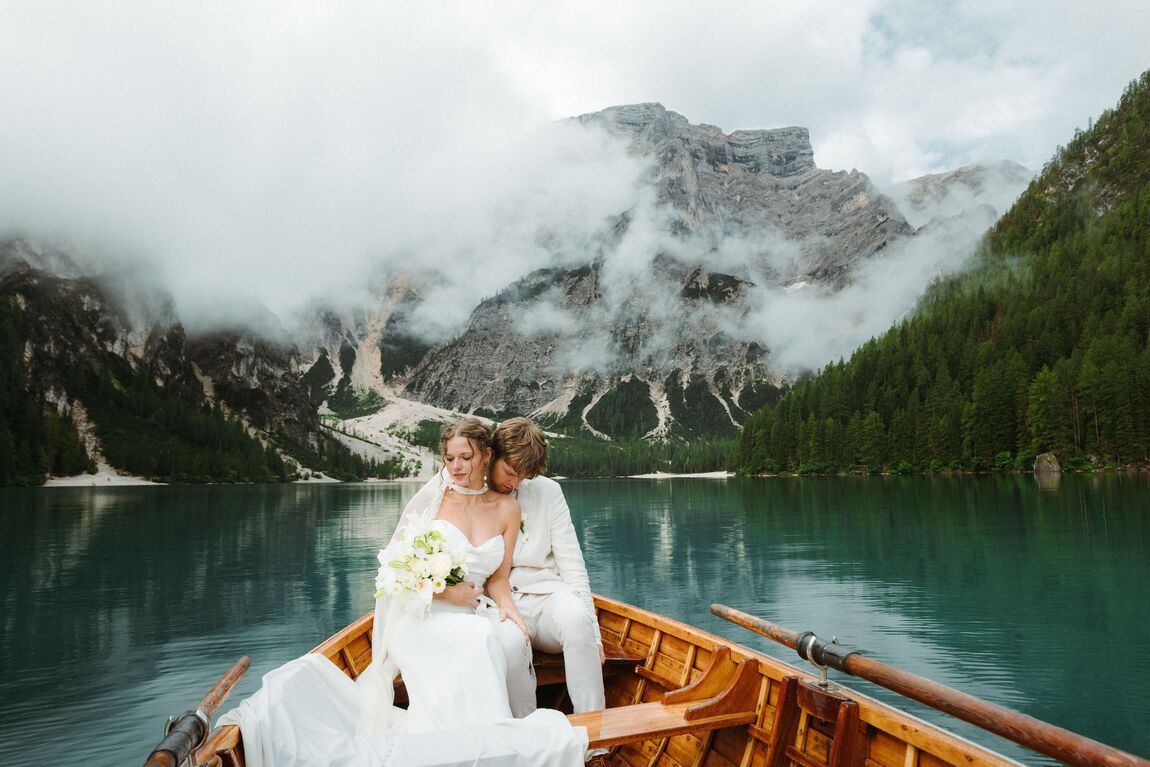 Bride and groom seated in a wooden boat on a mountain lake