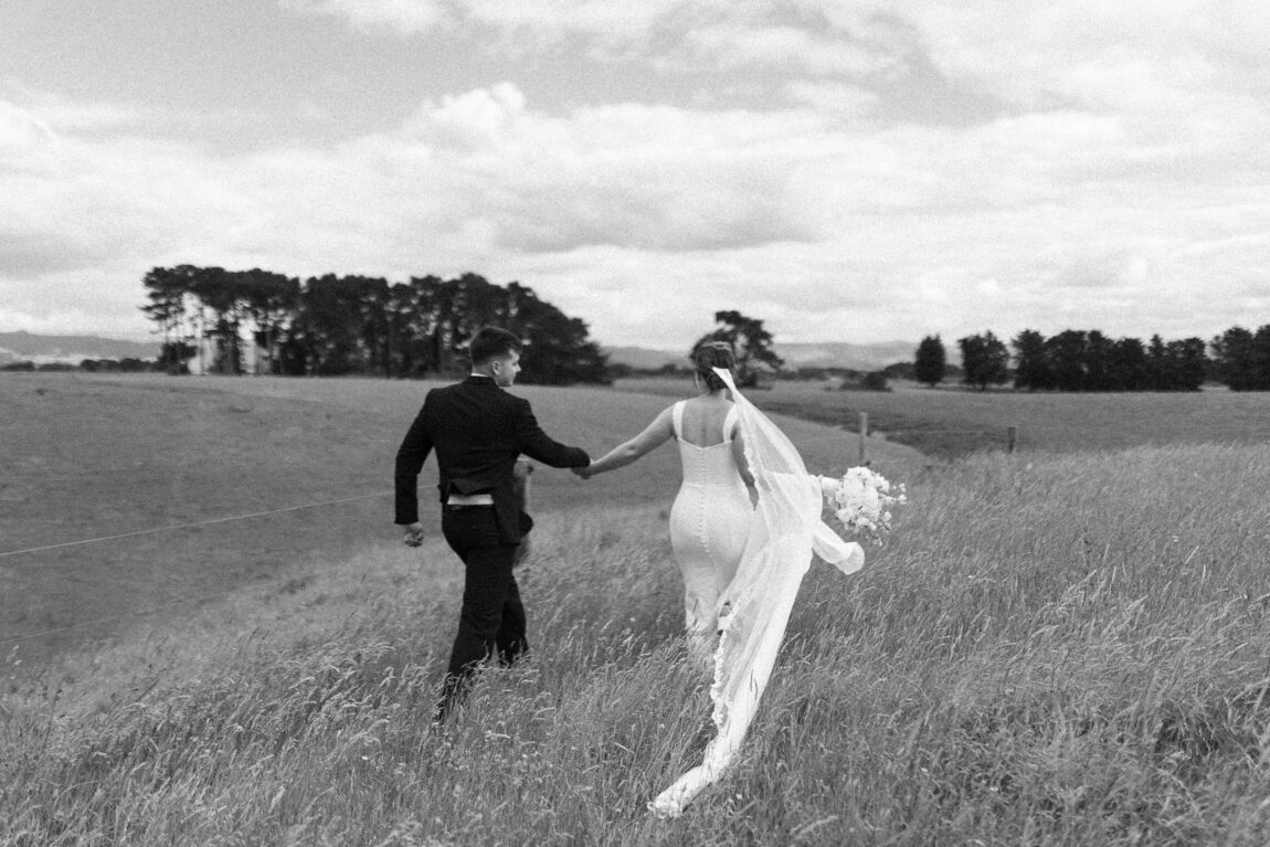 Bride and groom walking through a field, black and white